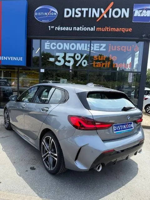 BMW Série 1 118d gris foncé vue 3/4 arrière droit, avec jantes alliage et feux arrière LED distinctifs.