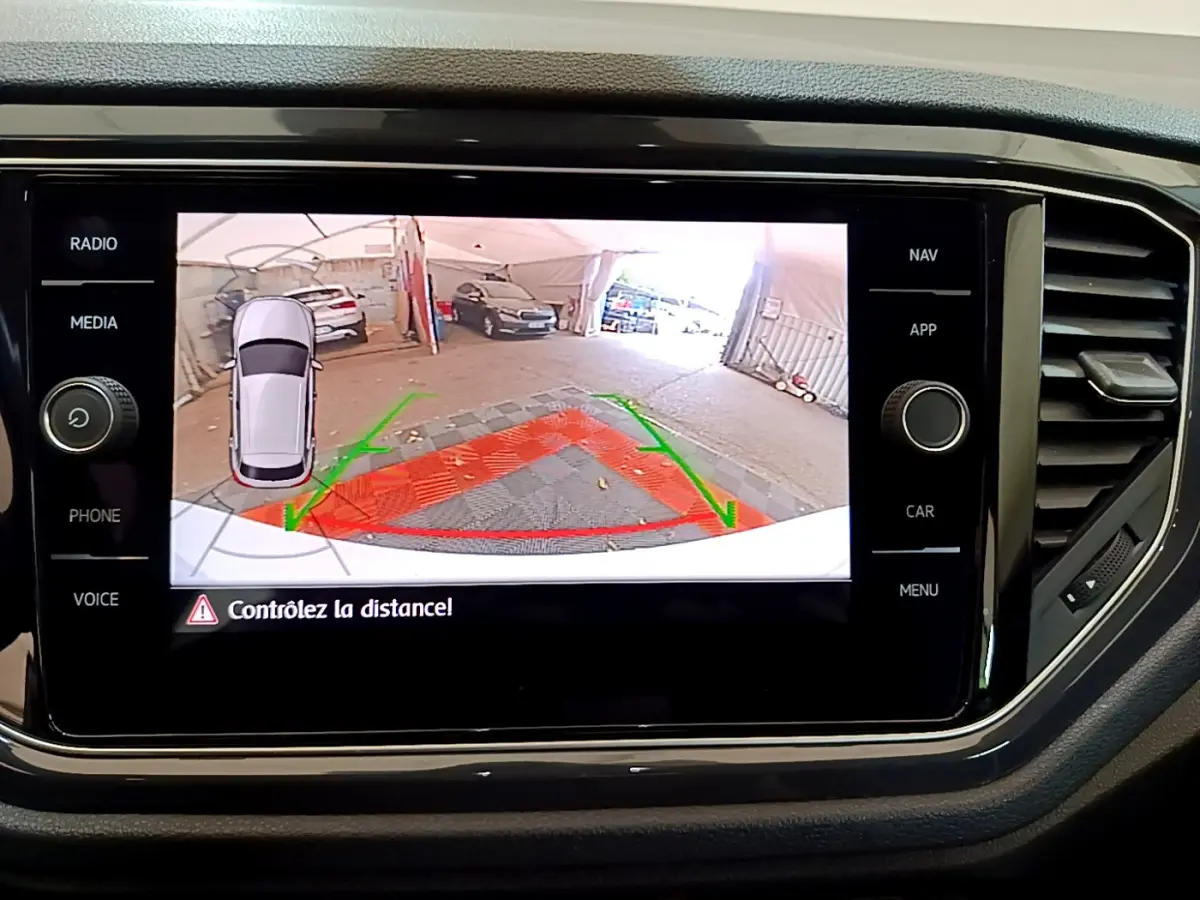 Écran tactile du Volkswagen T-Roc blanc montrant la caméra de recul avec guidage et alerte de distance.