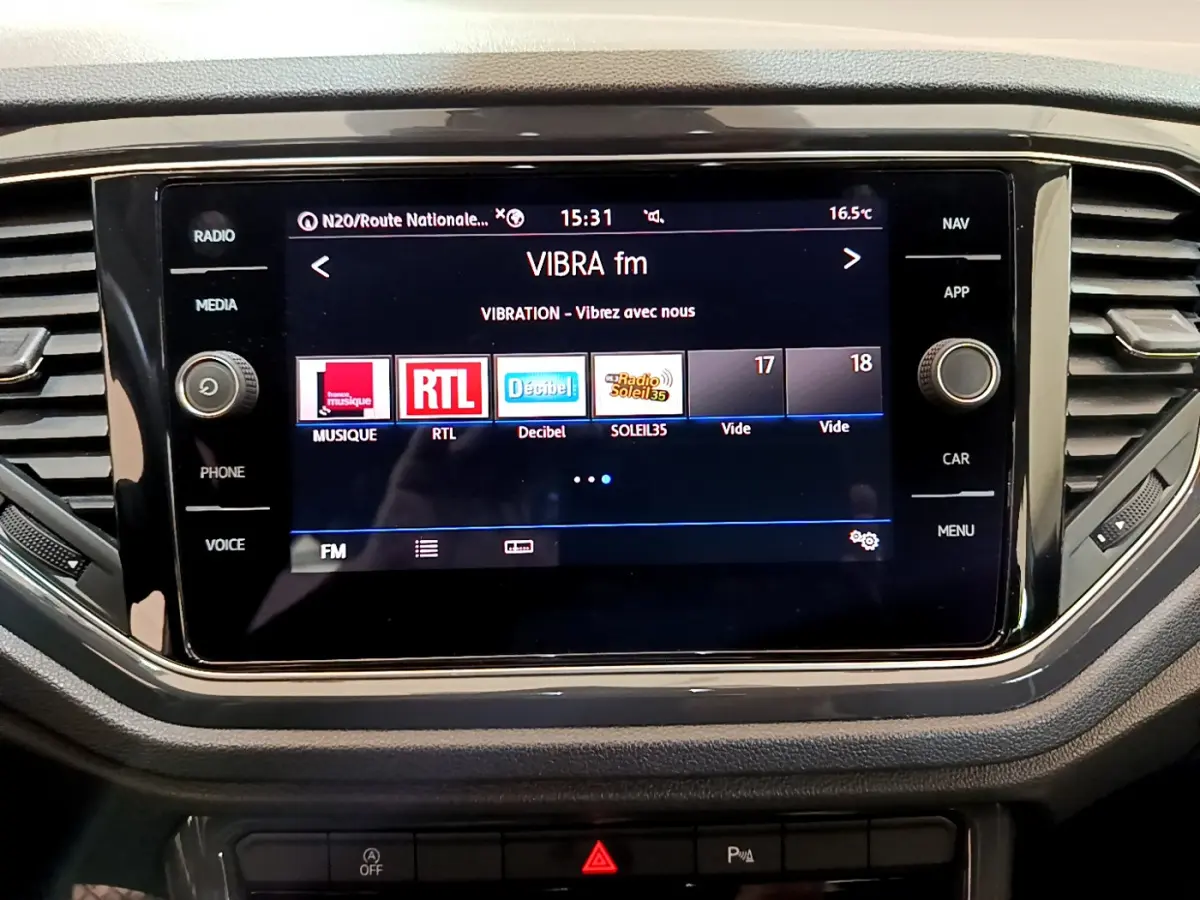 Écran tactile central allumé affichant les radios FM dans l’habitacle du Volkswagen T-Roc blanc.