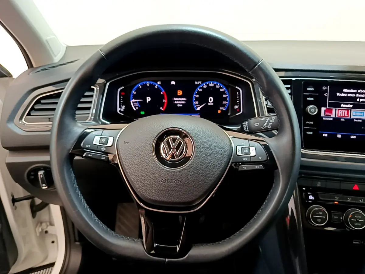 Vue rapprochée du volant cuir noir et du tableau de bord numérique du Volkswagen T-Roc blanc 2020.