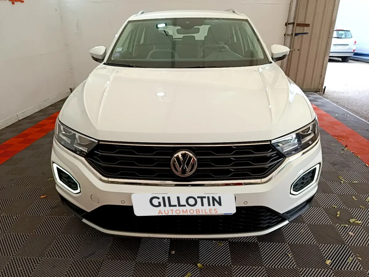 Vue frontale d'un Volkswagen T-Roc blanc avec feux LED allumés et calandre noire en intérieur garage.