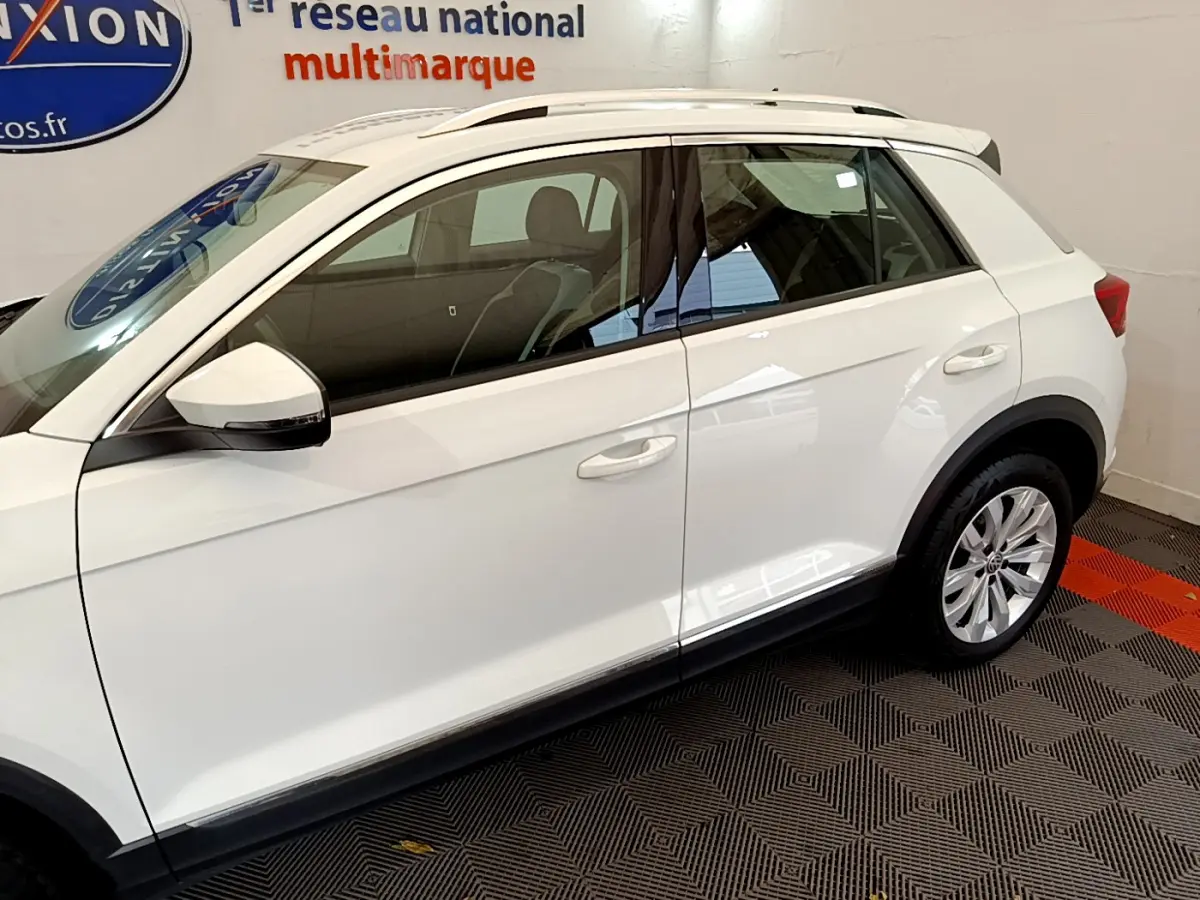 Vue latérale côté gauche d'un Volkswagen T-Roc blanc stationné en intérieur avec jantes alliage visibles.