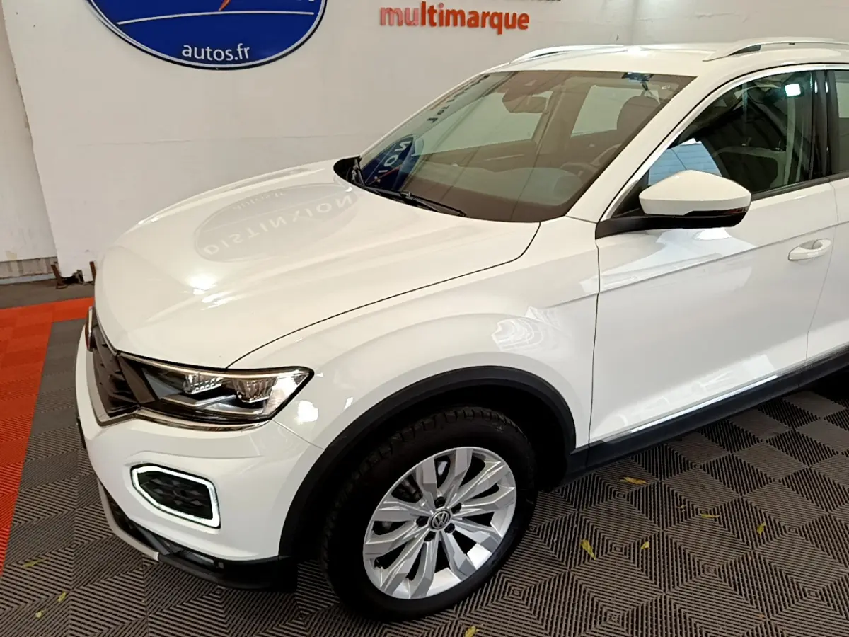 Vue 3/4 avant droit d'un Volkswagen T-Roc blanc avec phares LED et jantes alliage en intérieur showroom.