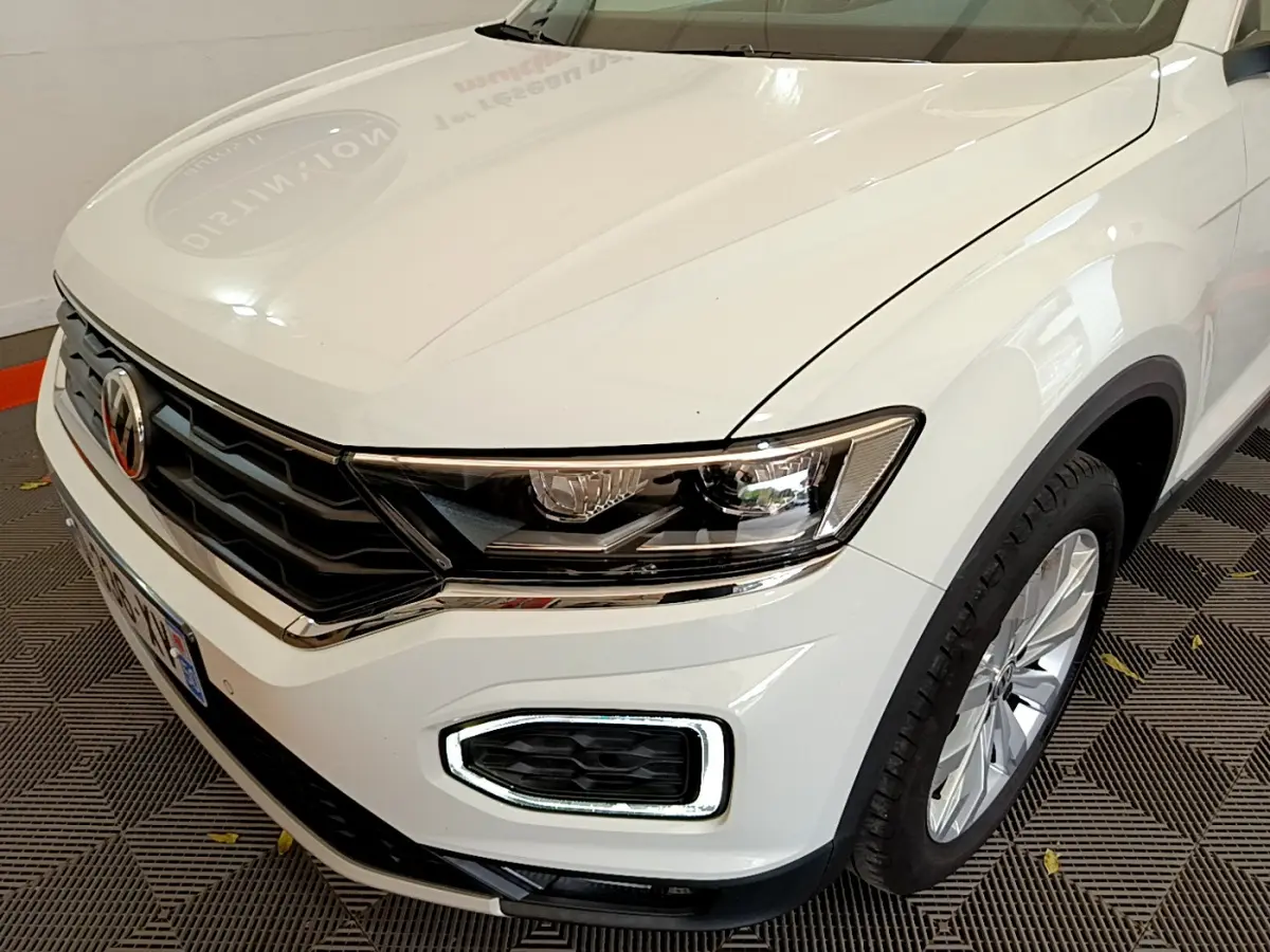 Vue 3/4 avant droit du Volkswagen T-Roc blanc, mettant en valeur ses phares LED et la calandre chromée.