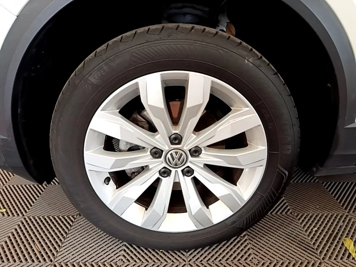 Gros plan sur la jante alliage argentée avec logo Volkswagen du Volkswagen T-Roc blanc, roue avant droite visible.