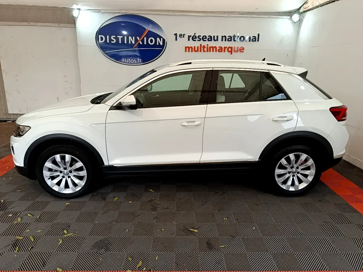 Profil droit d'un Volkswagen T-Roc blanc 2020, SUV compact avec jantes alliage et rails de toit chromés visibles.