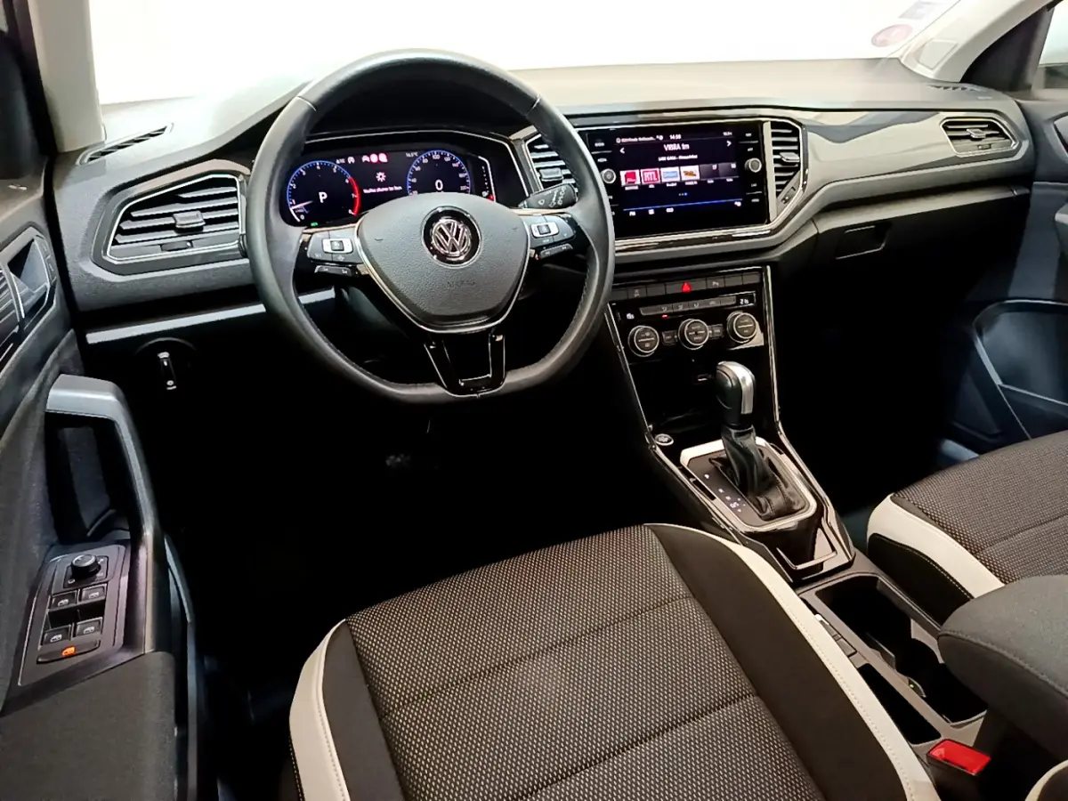 Vue intérieure du tableau de bord et volant cuir noir du Volkswagen T-Roc 1.5 TSI 150 EVO Carat avec écran tactile central.