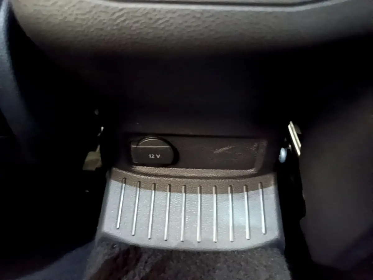 Prise 12V noire en gros plan sous le tableau de bord du Volkswagen T-Roc blanc, intérieur sombre.