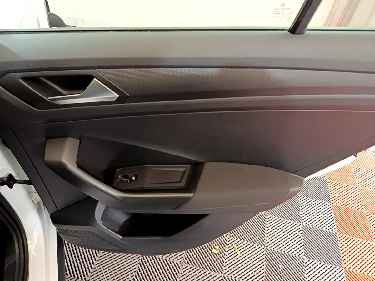 Vue intérieure côté gauche de la porte avant d'un Volkswagen T-Roc blanc, avec poignée et commande de vitre noire.