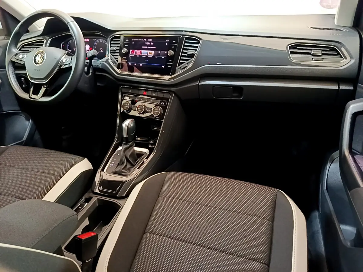 Intérieur avant du Volkswagen T-Roc 1.5 TSI blanc, tableau de bord moderne avec écran tactile et sièges bi-ton noirs et beige.
