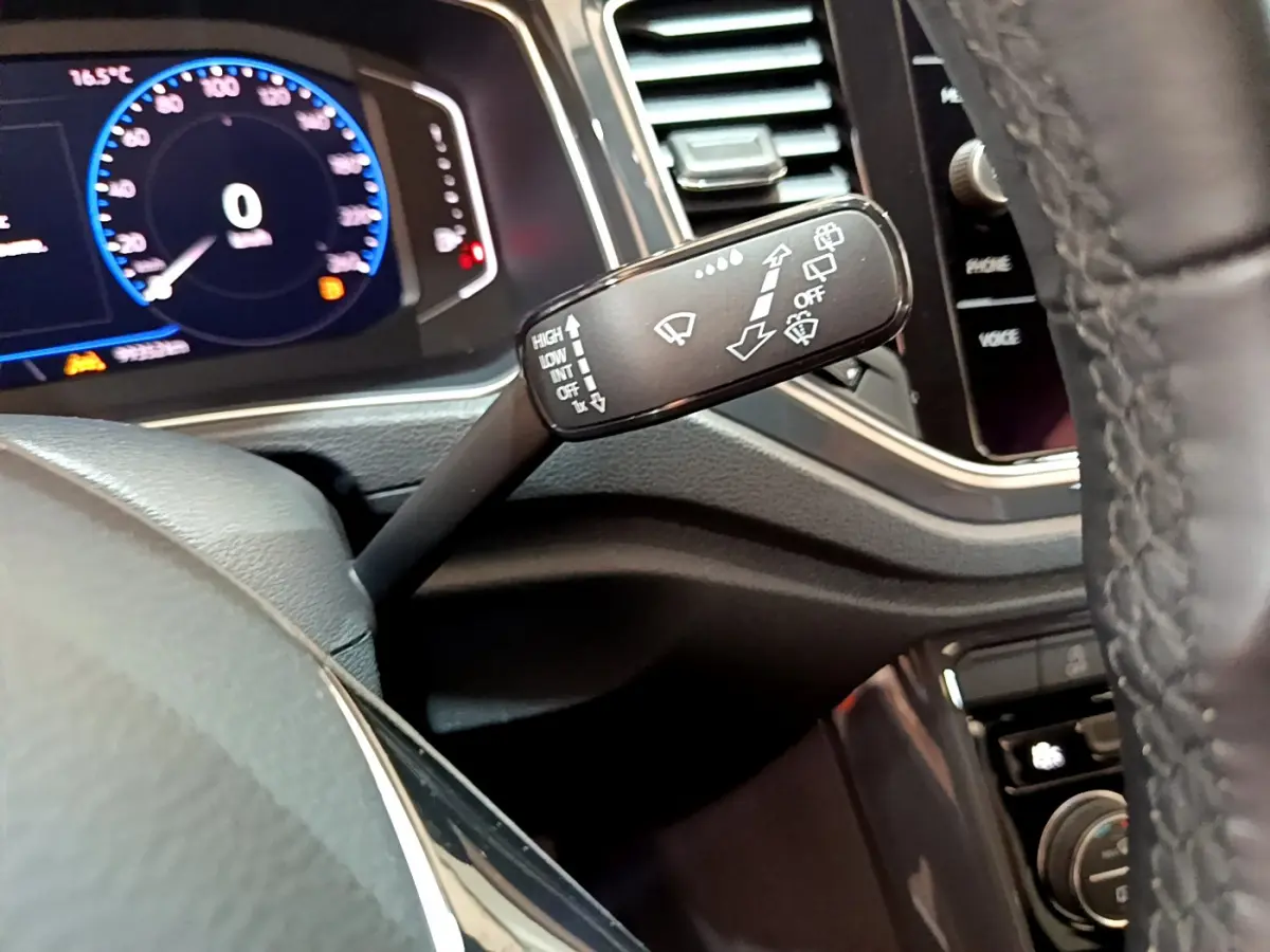 Gros plan sur la commande d’essuie-glace à gauche du volant cuir du tableau de bord numérique du Volkswagen T-Roc blanc.