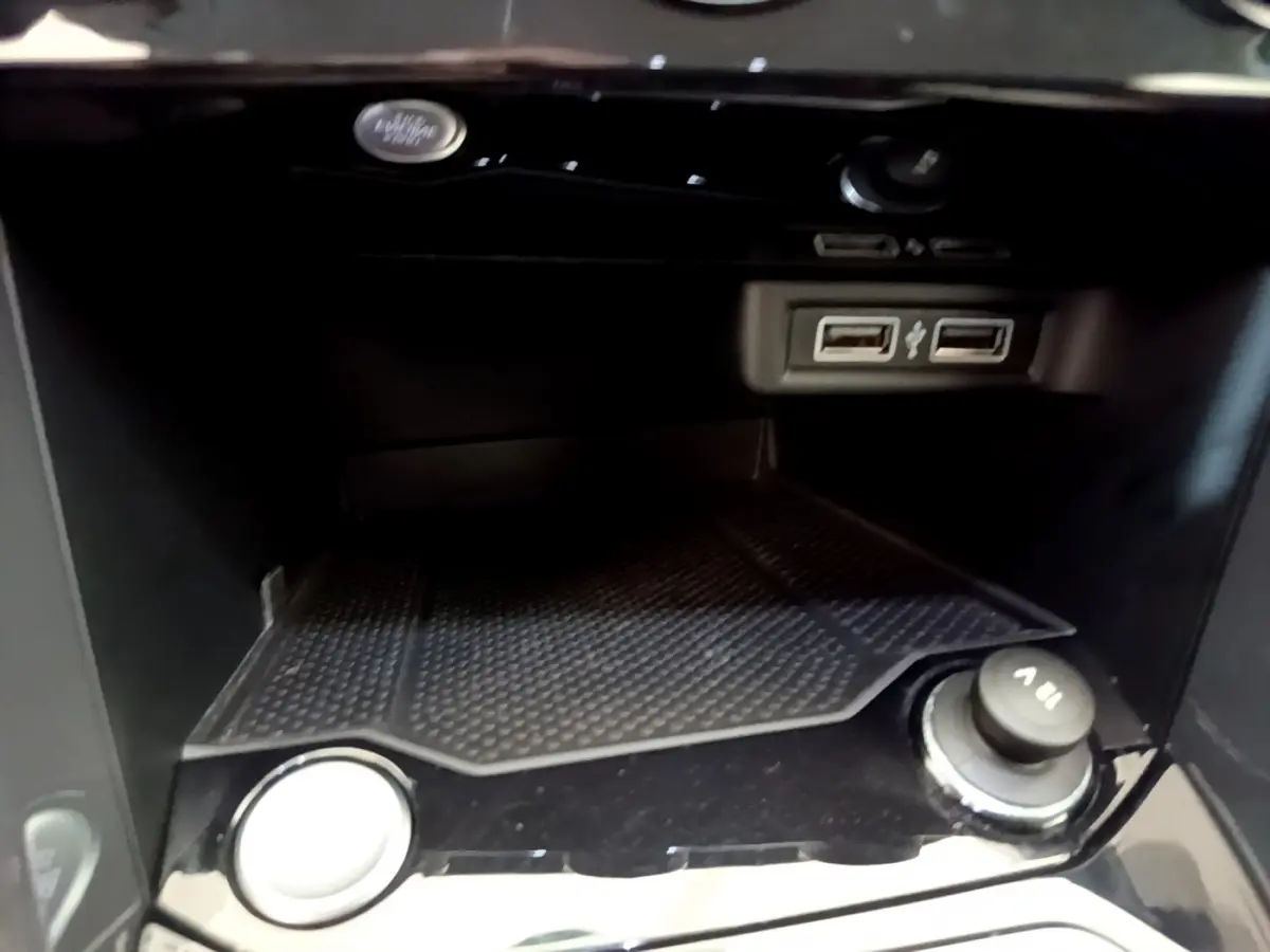 Gros plan sur la console centrale noire du Volkswagen T-Roc blanc, montrant les ports USB et la prise 12V.