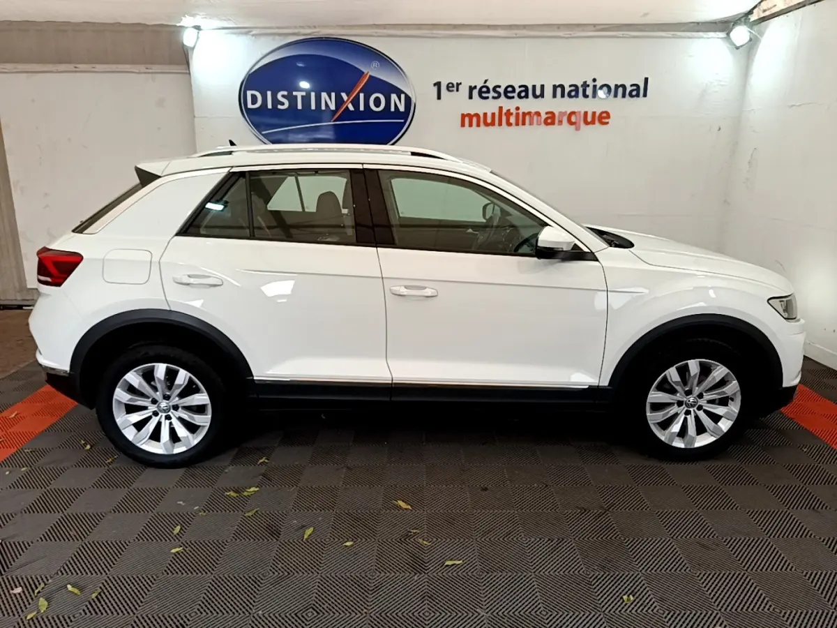 Profil droit du Volkswagen T-Roc blanc 2020 avec jantes alliage et barres de toit chromées en intérieur showroom.
