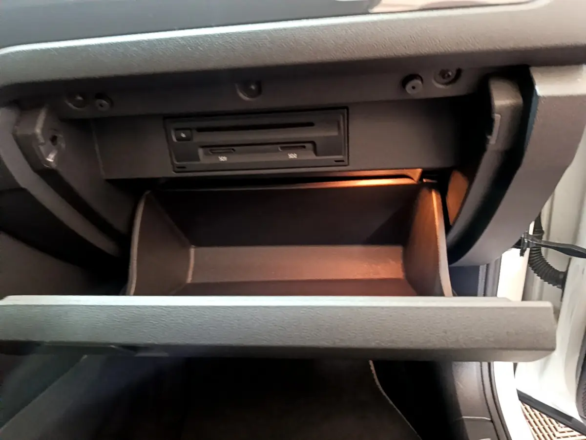 Vue rapprochée de la boîte à gants ouverte du Volkswagen T-Roc blanc, éclairage intérieur orange visible.