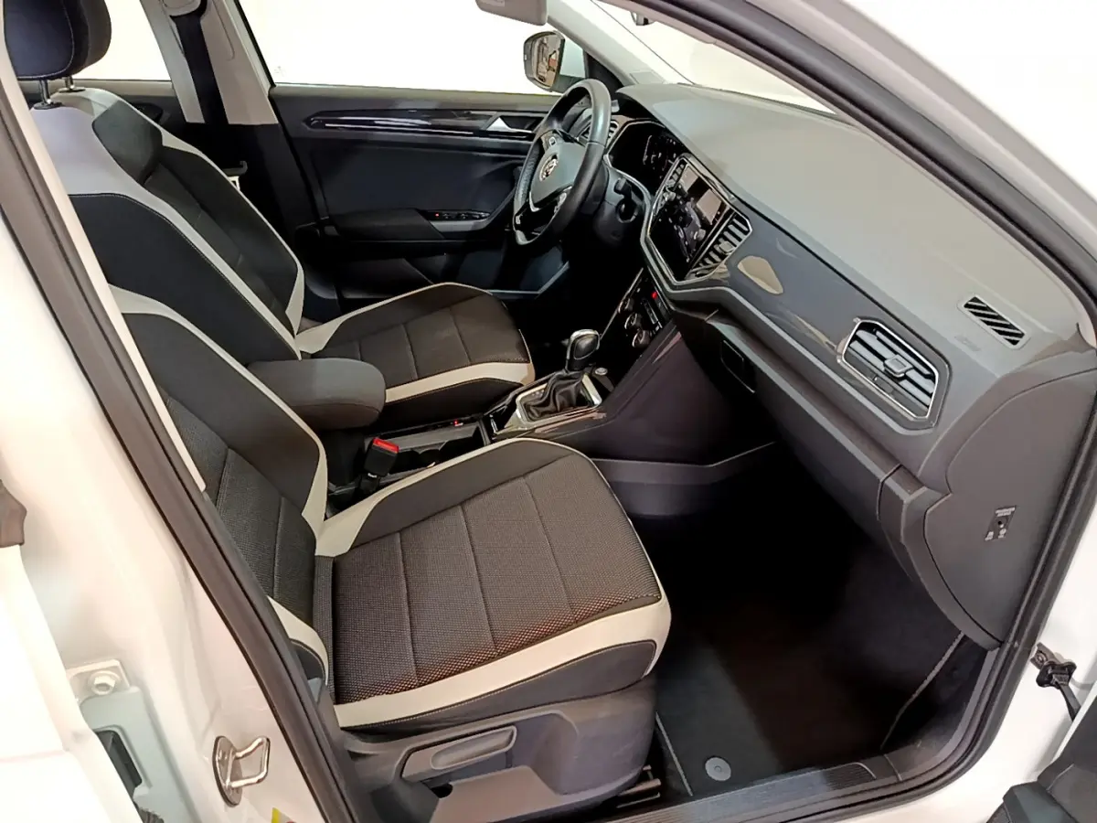 Intérieur du Volkswagen T-Roc blanc vu côté conducteur, sièges bi-ton noirs et gris, tableau de bord moderne avec écran tactile.