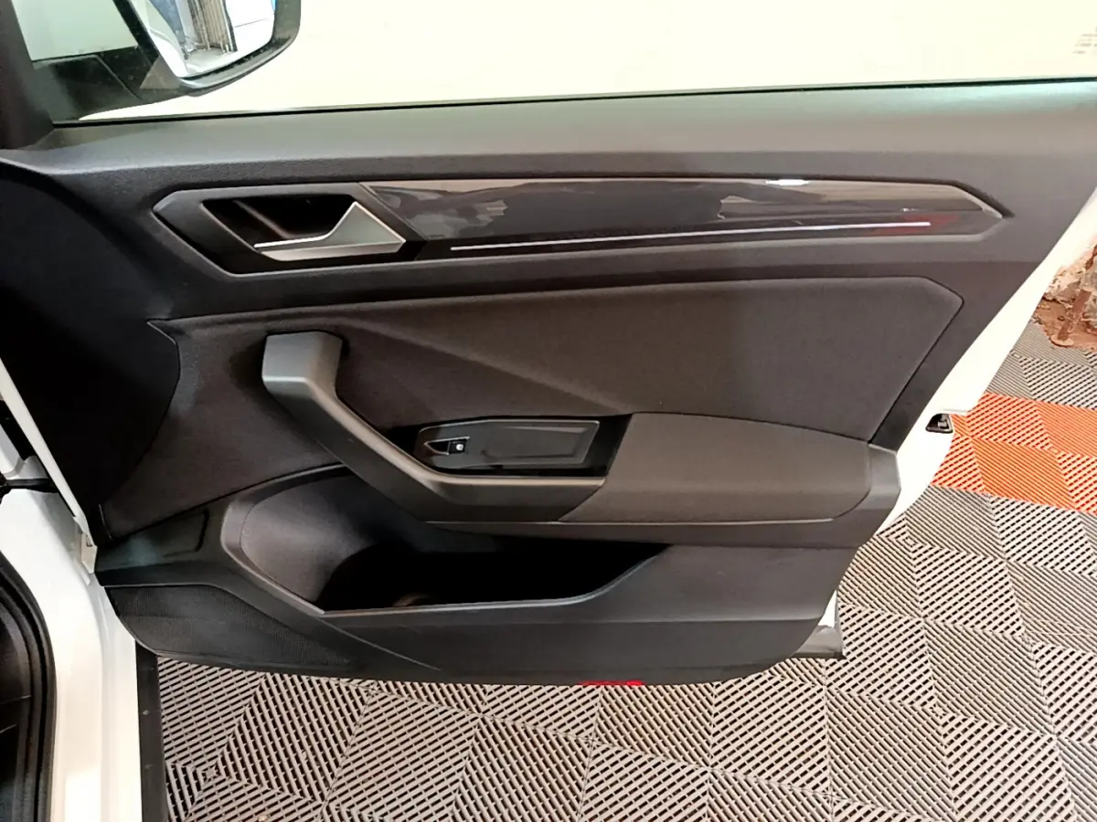 Intérieur côté conducteur de la porte d'une Volkswagen T-Roc blanche, avec poignée et panneau noir mat.