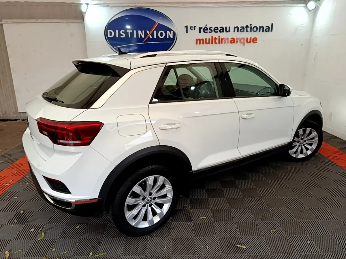 Volkswagen T-Roc blanc vu de trois quarts arrière droit, avec jantes alliage et toit ouvrant visible.