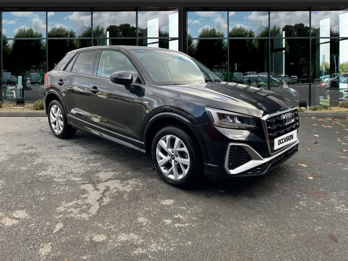 Audi Q2 noir en vue 3/4 avant droit, avec calandre marquée et jantes argentées, stationné devant un bâtiment vitré.