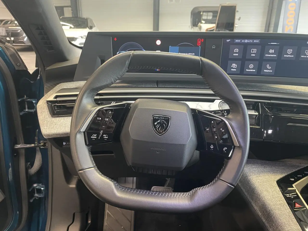 Vue intérieure centrée sur le volant cuir noir du Peugeot 5008 Bleu Obsession avec tableau de bord numérique panoramique.