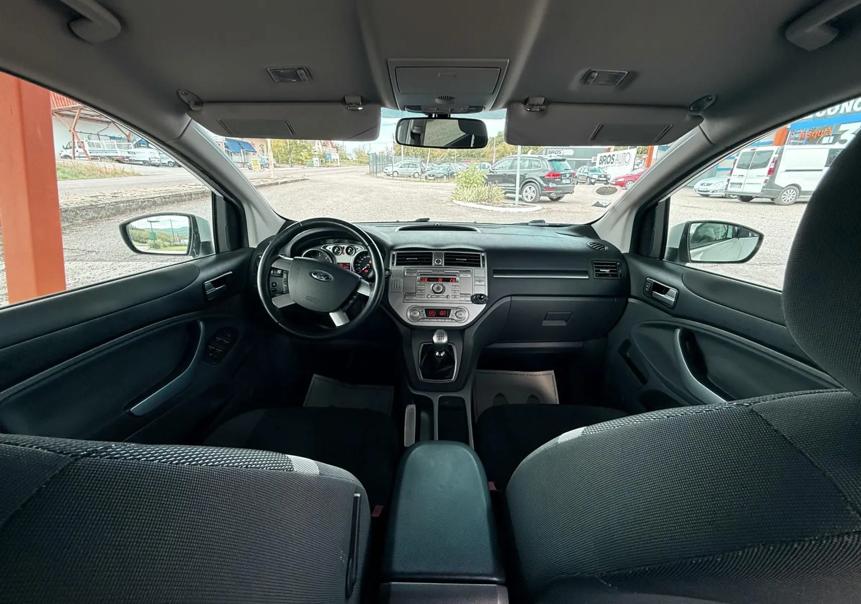 Intérieur avant d'une Ford Kuga blanc 2012, vue du tableau de bord et volant côté gauche avec sièges tissu gris noir.