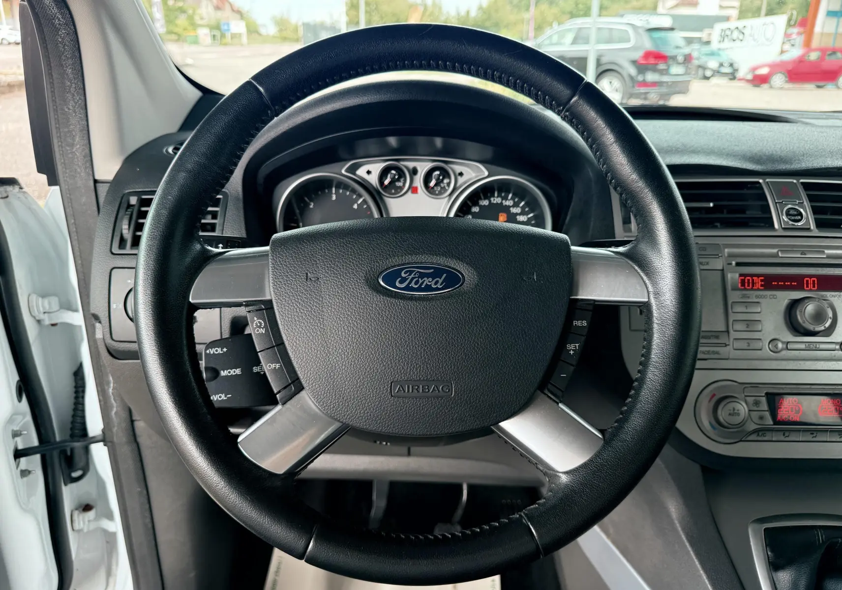 Vue intérieure centrée sur le volant noir du Ford Kuga blanc 2012 avec tableau de bord et commandes visibles.