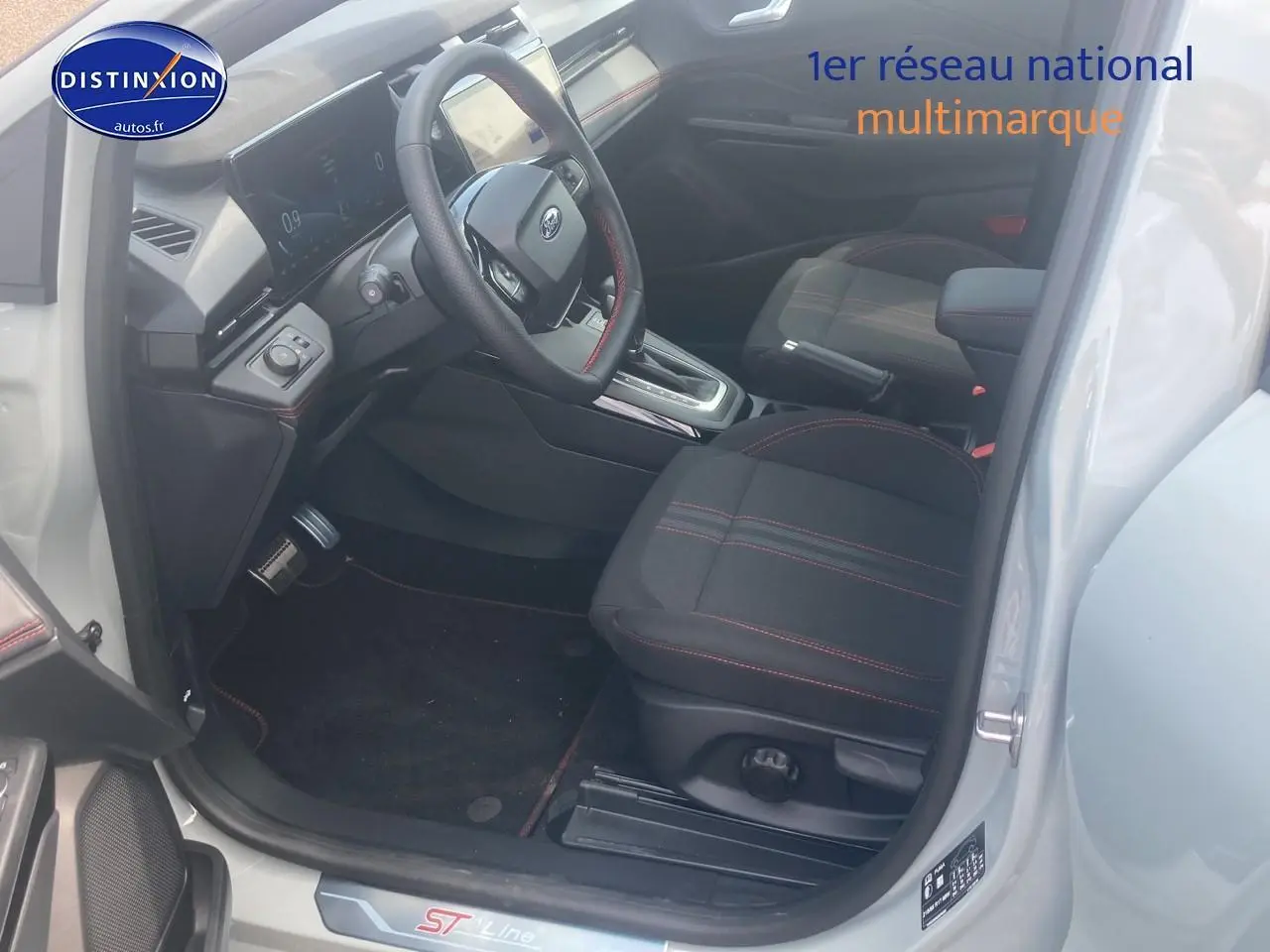 Intérieur avant droit du Ford Puma gris cactus 2025, sièges tissu noirs avec surpiqûres rouges et volant multifonction.