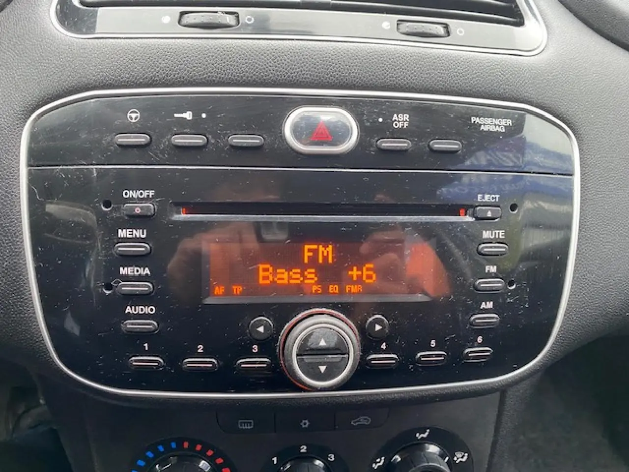 Gros plan sur la console centrale de la Fiat Grande Punto 2015, affichant l'autoradio FM avec réglage des basses à +6.