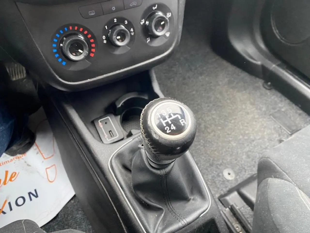 Gros plan sur le levier de vitesse manuel et les commandes de climatisation d'une Fiat Grande Punto gris métallisé.