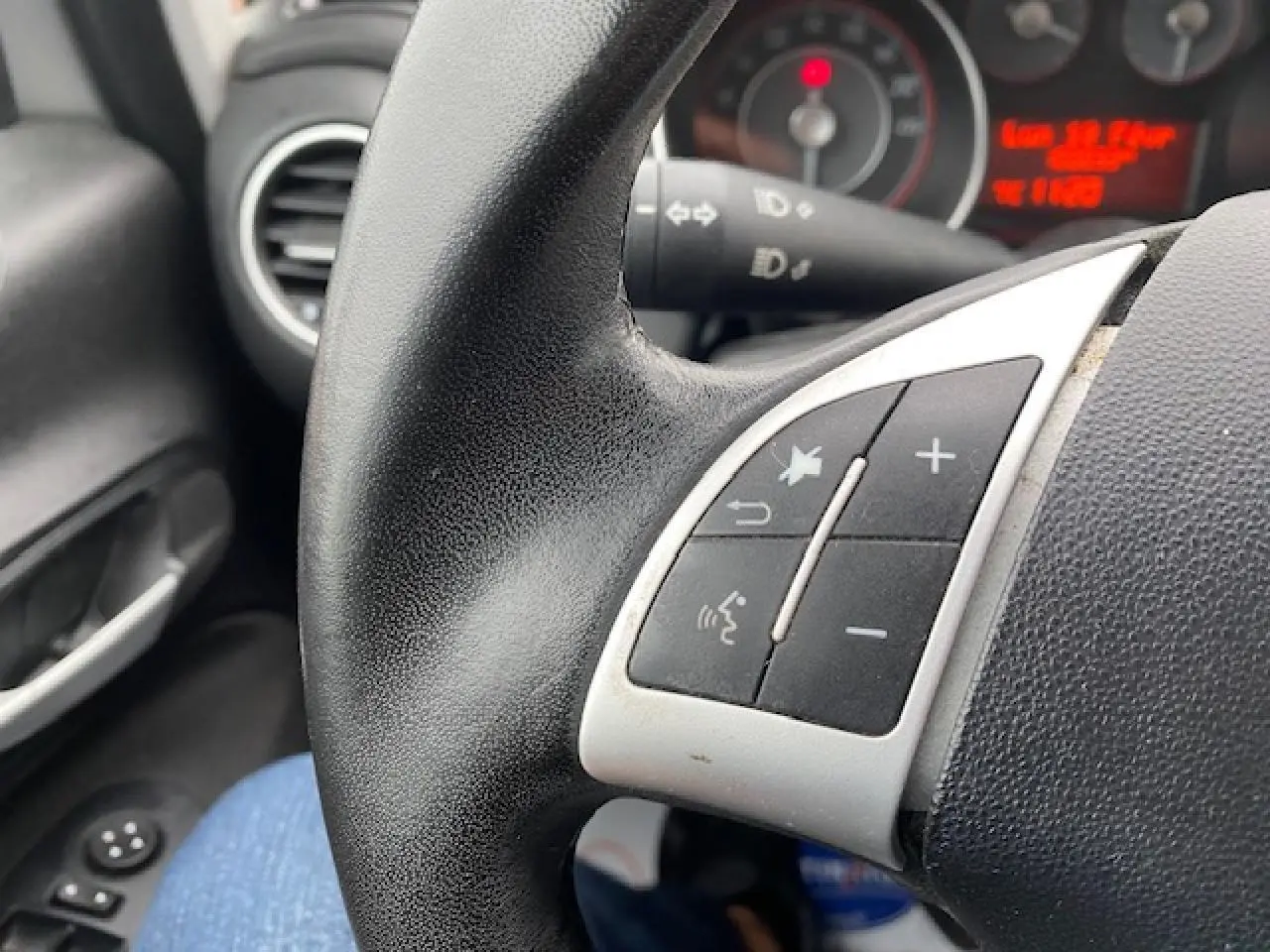 Gros plan sur les commandes au volant noir de la Fiat Grande Punto gris, avec tableau de bord et aérateur en arrière-plan.