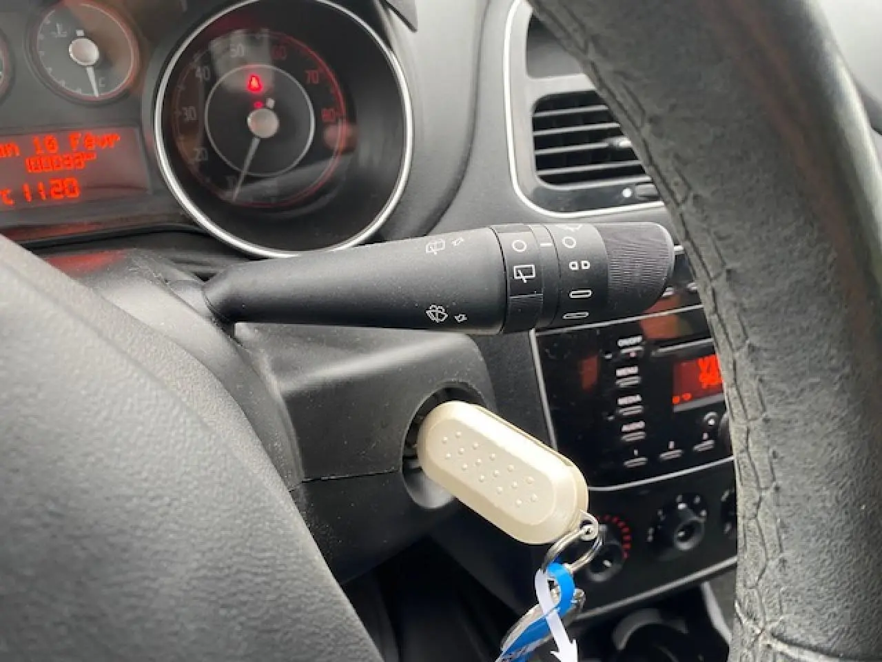 Vue rapprochée du tableau de bord et du volant d'une Fiat Grande Punto gris, avec clé insérée et commandes visibles.