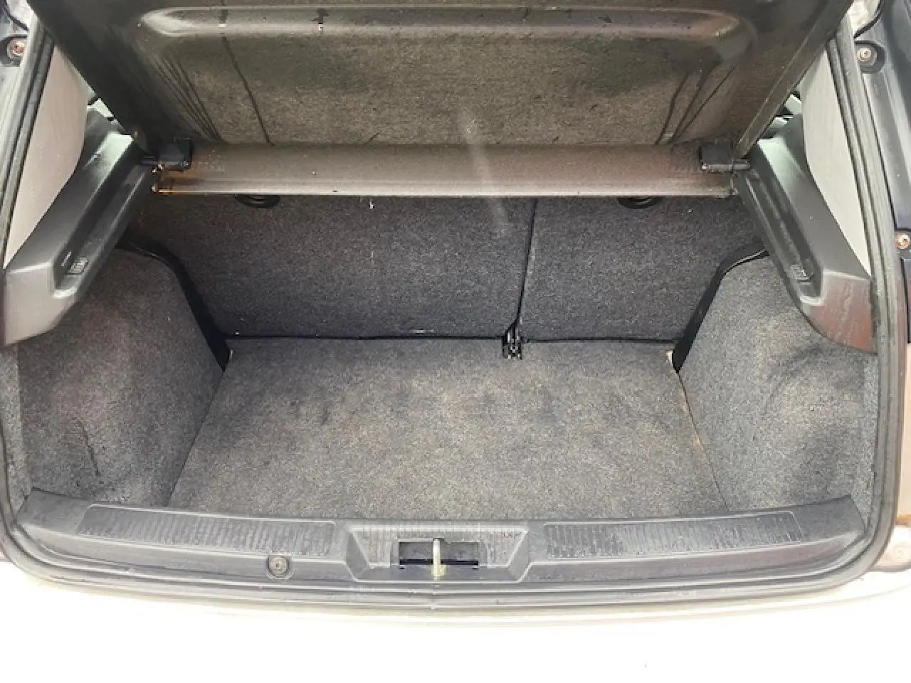 Coffre ouvert de la Fiat Grande Punto gris, vue de l'arrière montrant l'espace de chargement vide et la moquette intérieure.