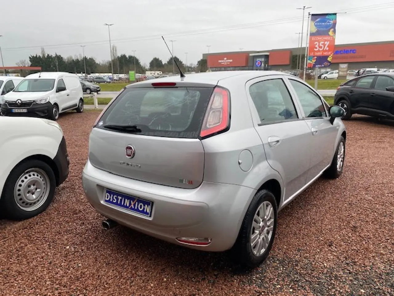 Vue 3/4 arrière droite d'une Fiat Grande Punto gris métallisé, avec feux arrière caractéristiques et antenne de toit.