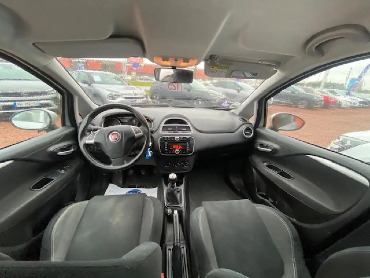 Intérieur noir de la Fiat Grande Punto 2015, vue frontale du tableau de bord avec volant multifonction et boîte manuelle.