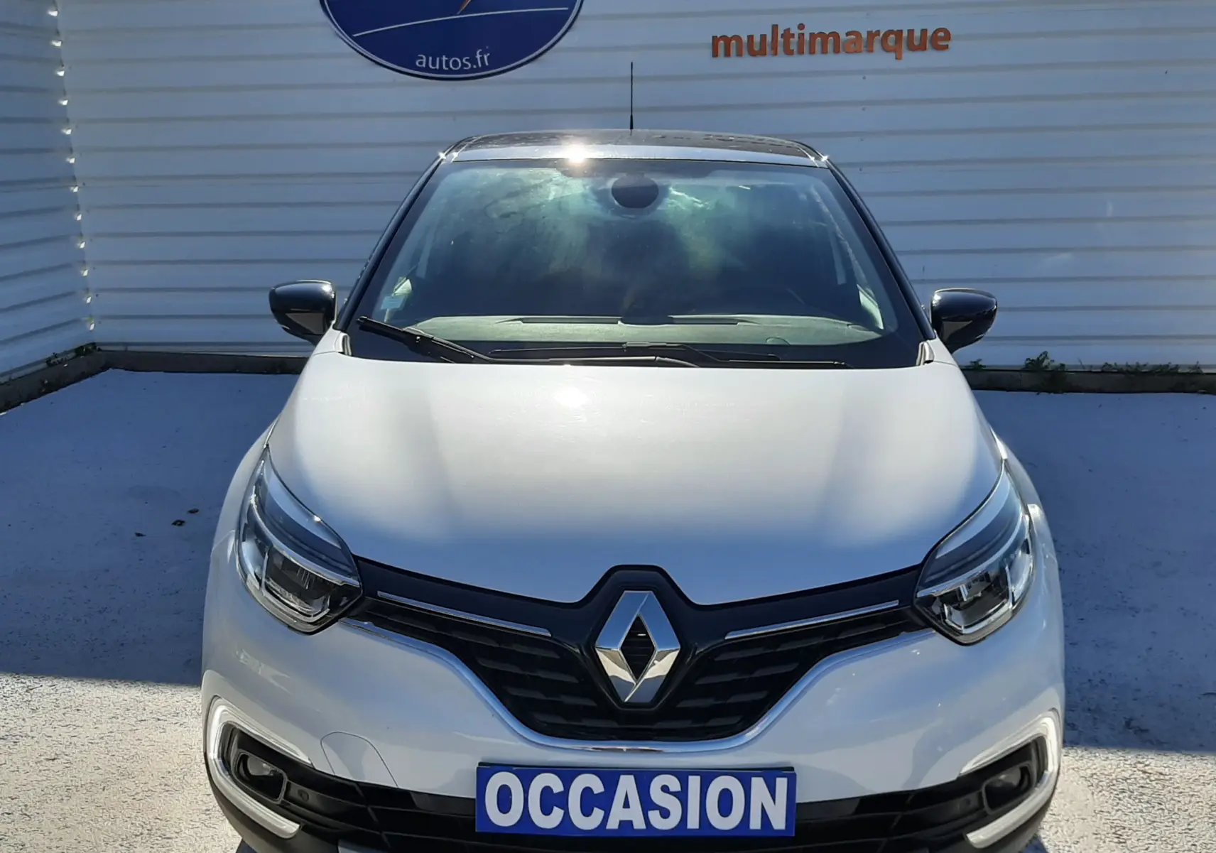 Vue frontale d'un Renault Captur blanc nacré avec toit noir, calandre noire et plaque "OCCASION" visible.