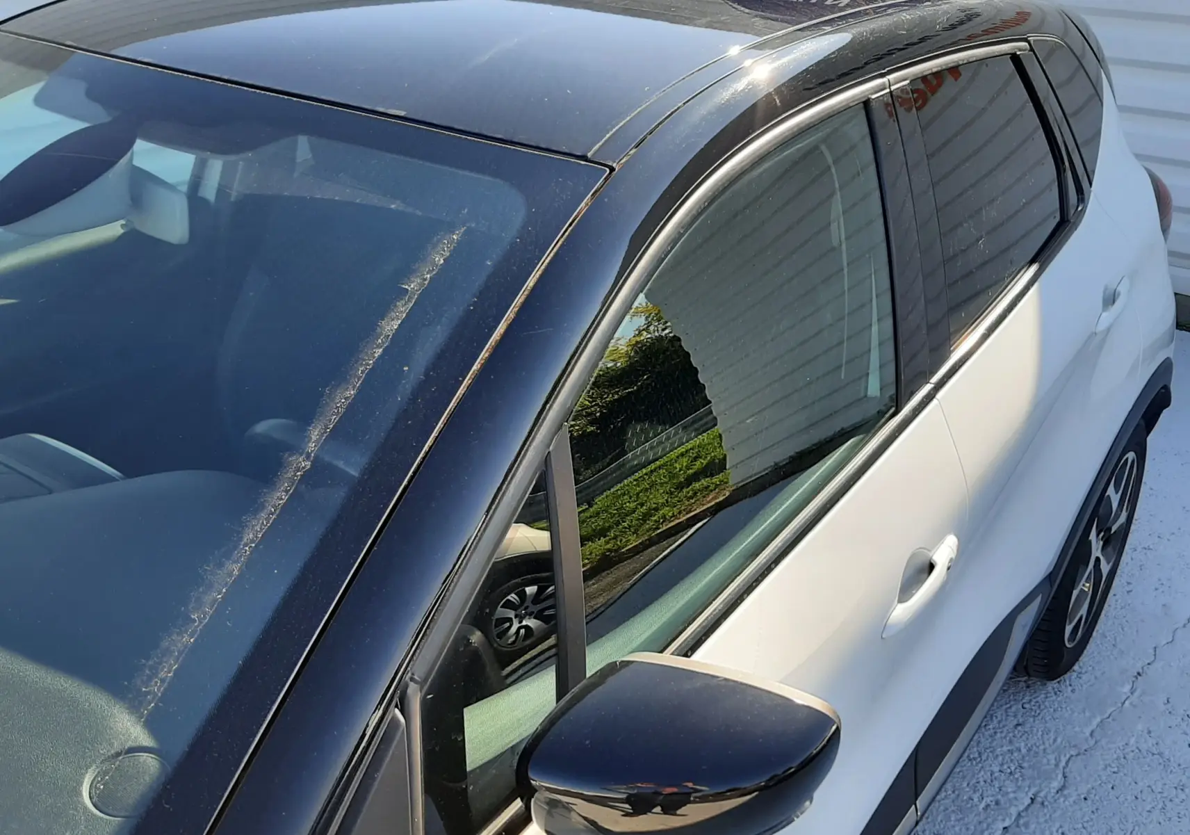 Vue plongeante côté gauche d'un Renault Captur blanc nacré avec toit noir brillant et rétroviseur assorti.