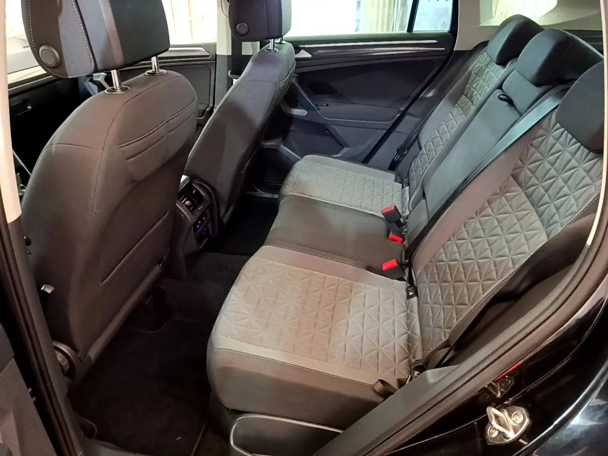 Vue intérieure côté droit des sièges arrière gris à motifs du Volkswagen Tiguan noir 2021, avec accoudoir et ceintures visibles.