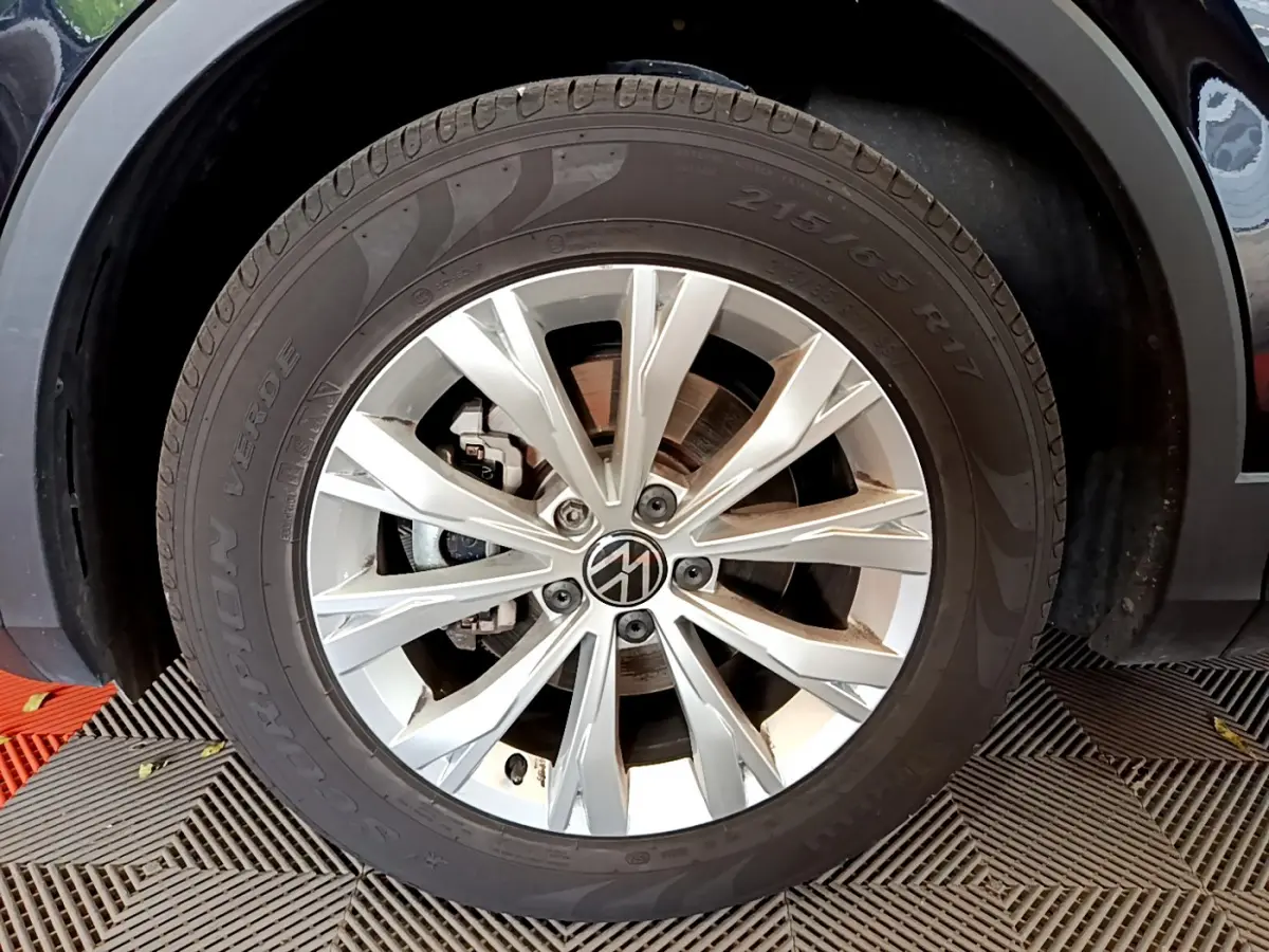 Gros plan sur la roue avant droite du Volkswagen Tiguan noir, avec jante alliage argentée et logo VW central.