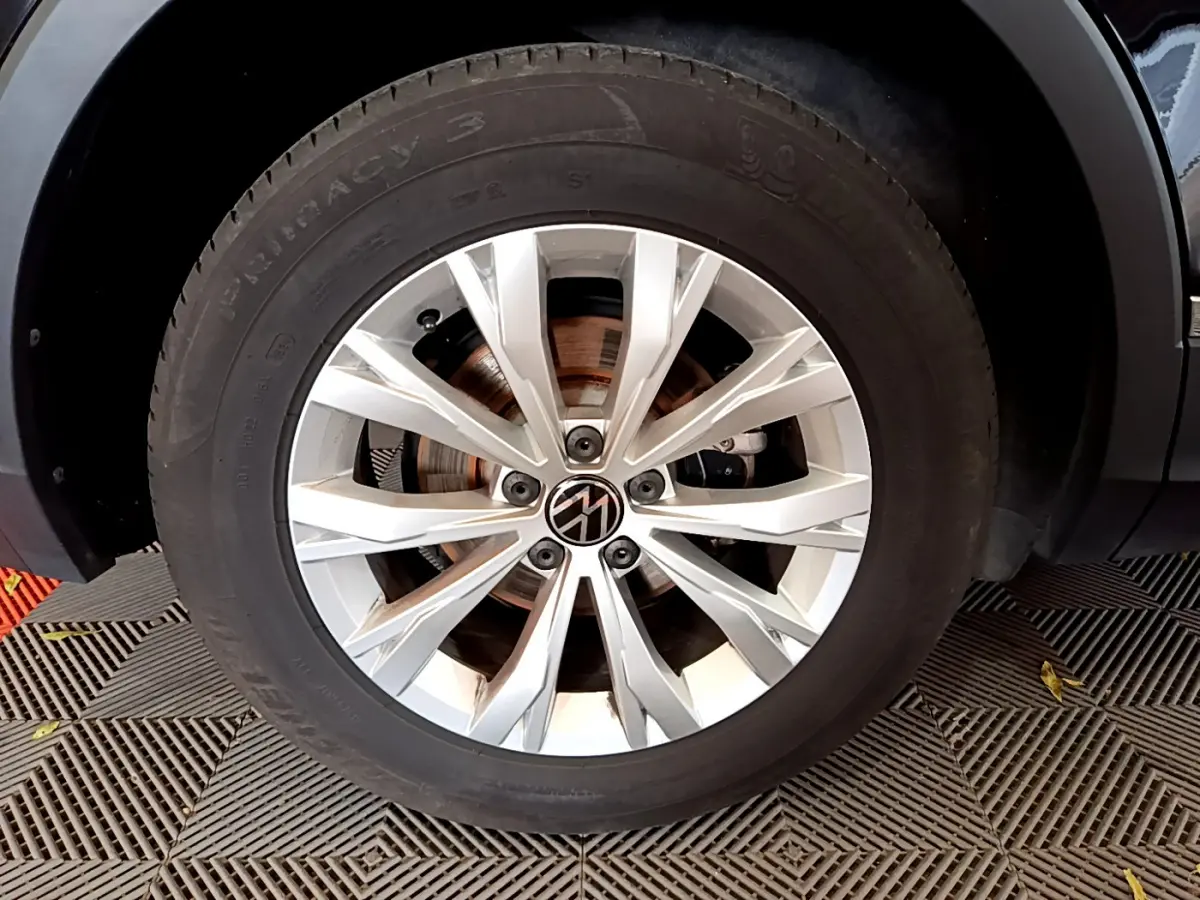 Gros plan sur la roue avant droite du Volkswagen Tiguan noir, mettant en valeur la jante argentée au design moderne.