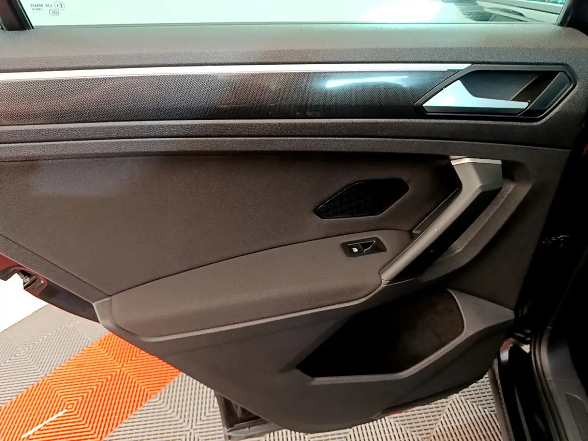 Porte intérieure côté gauche noire du Volkswagen Tiguan 2021 avec poignée argentée et bouton de verrouillage.