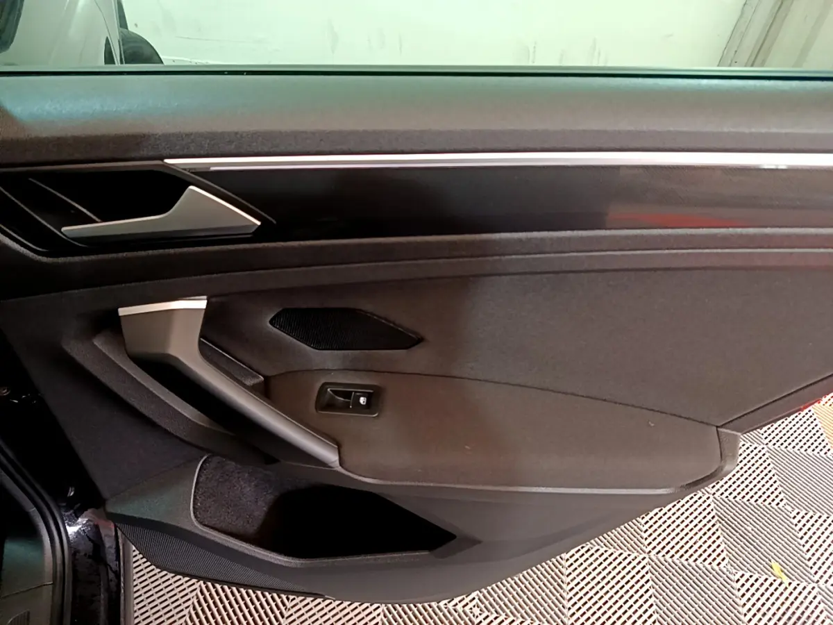 Détail de la porte côté gauche noire du Volkswagen Tiguan 2.0 TDI 150 DSG7 avec poignée argentée et haut-parleur intégré.