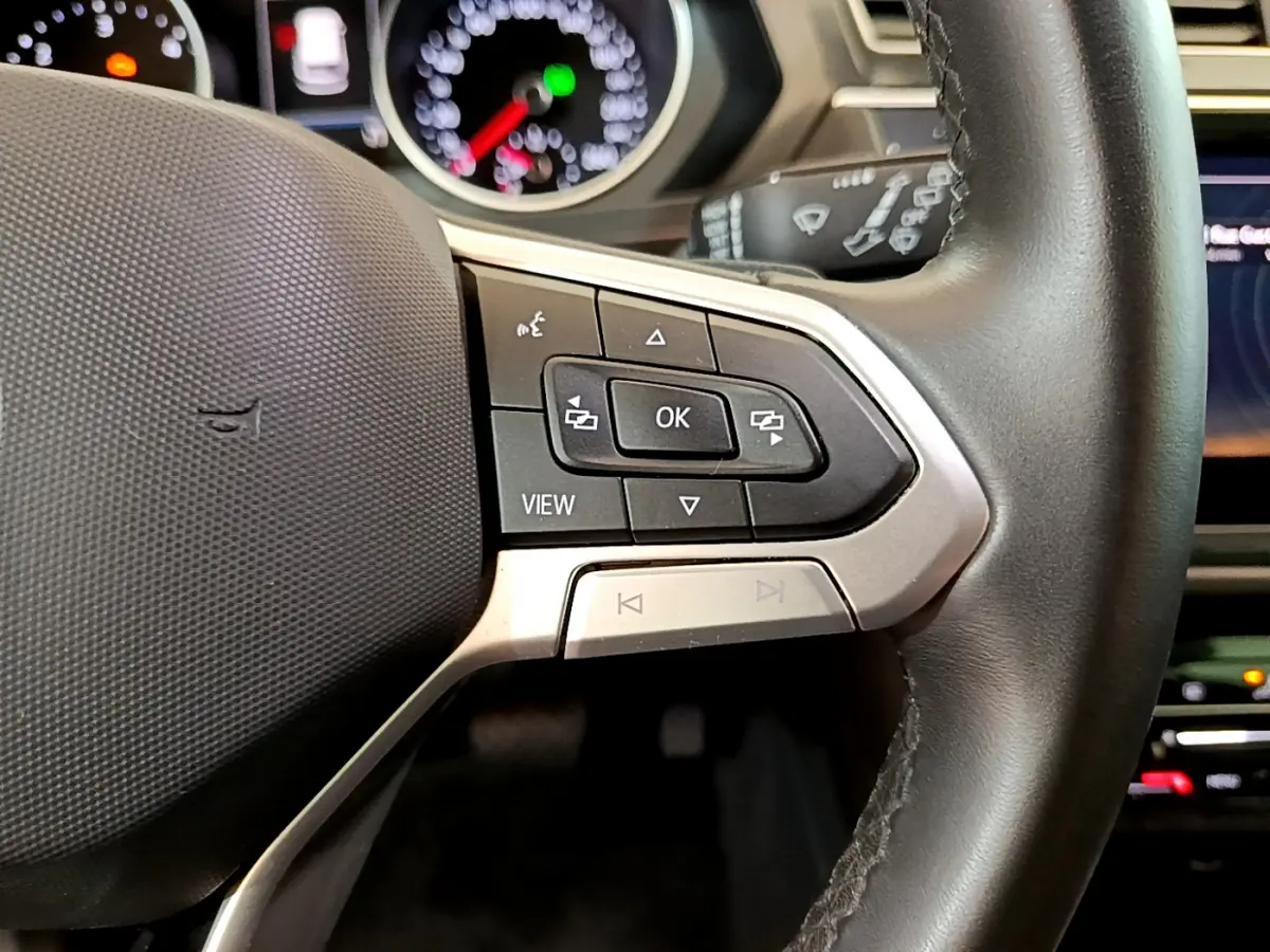 Gros plan sur les commandes au volant côté droit du Volkswagen Tiguan 2.0 TDI noir, avec tableau de bord lumineux en arrière-plan.