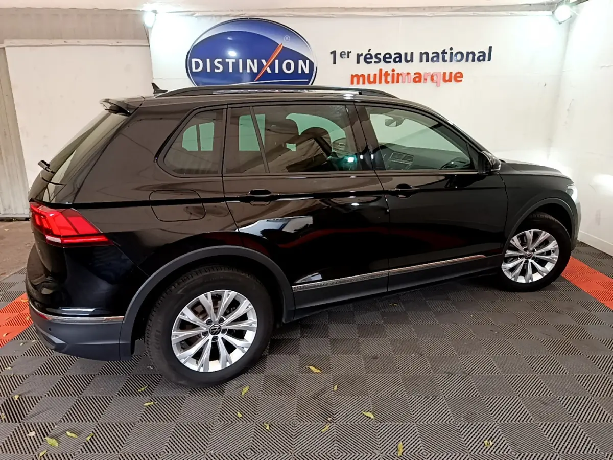 Volkswagen Tiguan noir 2021 vu de profil côté gauche, avec jantes alliage et toit noir brillant en intérieur showroom.