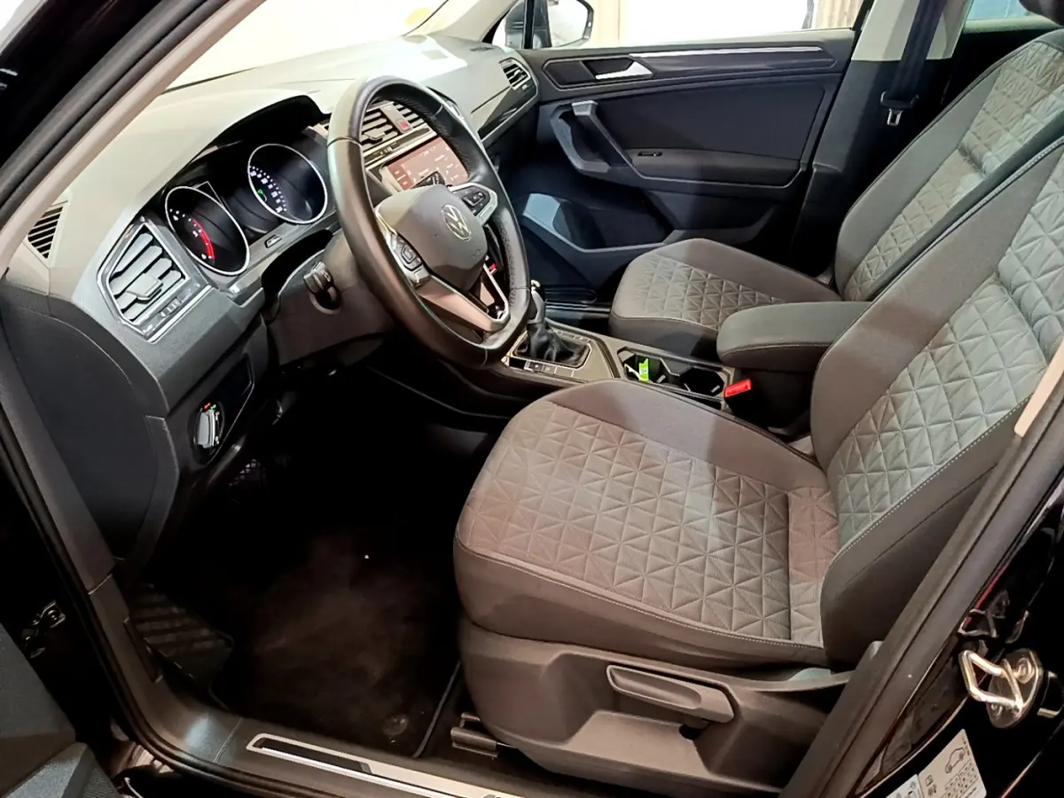 Intérieur avant droit du Volkswagen Tiguan noir 2021, sièges gris à motifs, volant cuir et tableau de bord tactile.