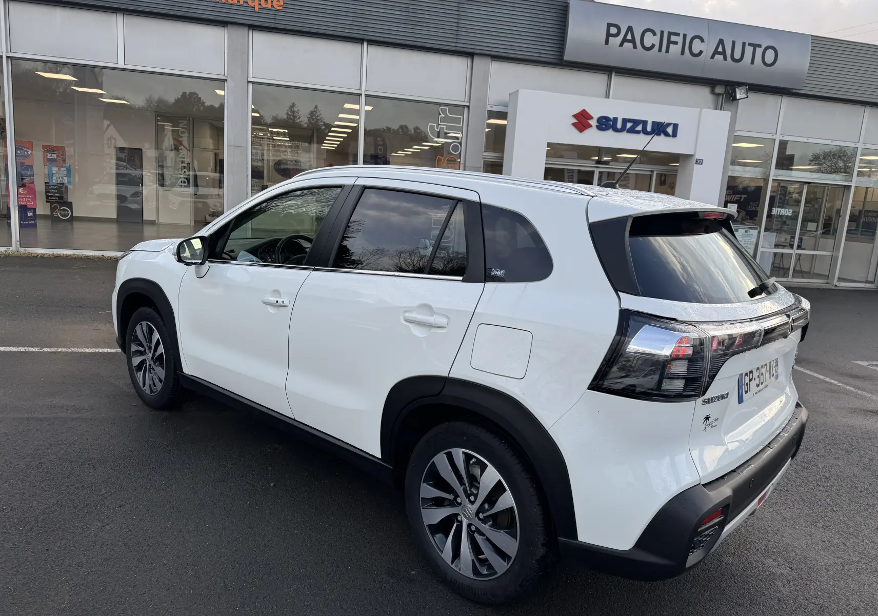 Suzuki S-Cross blanc 2023 vu en 3/4 arrière droit, avec feux arrière noirs et jantes alliage distinctives.