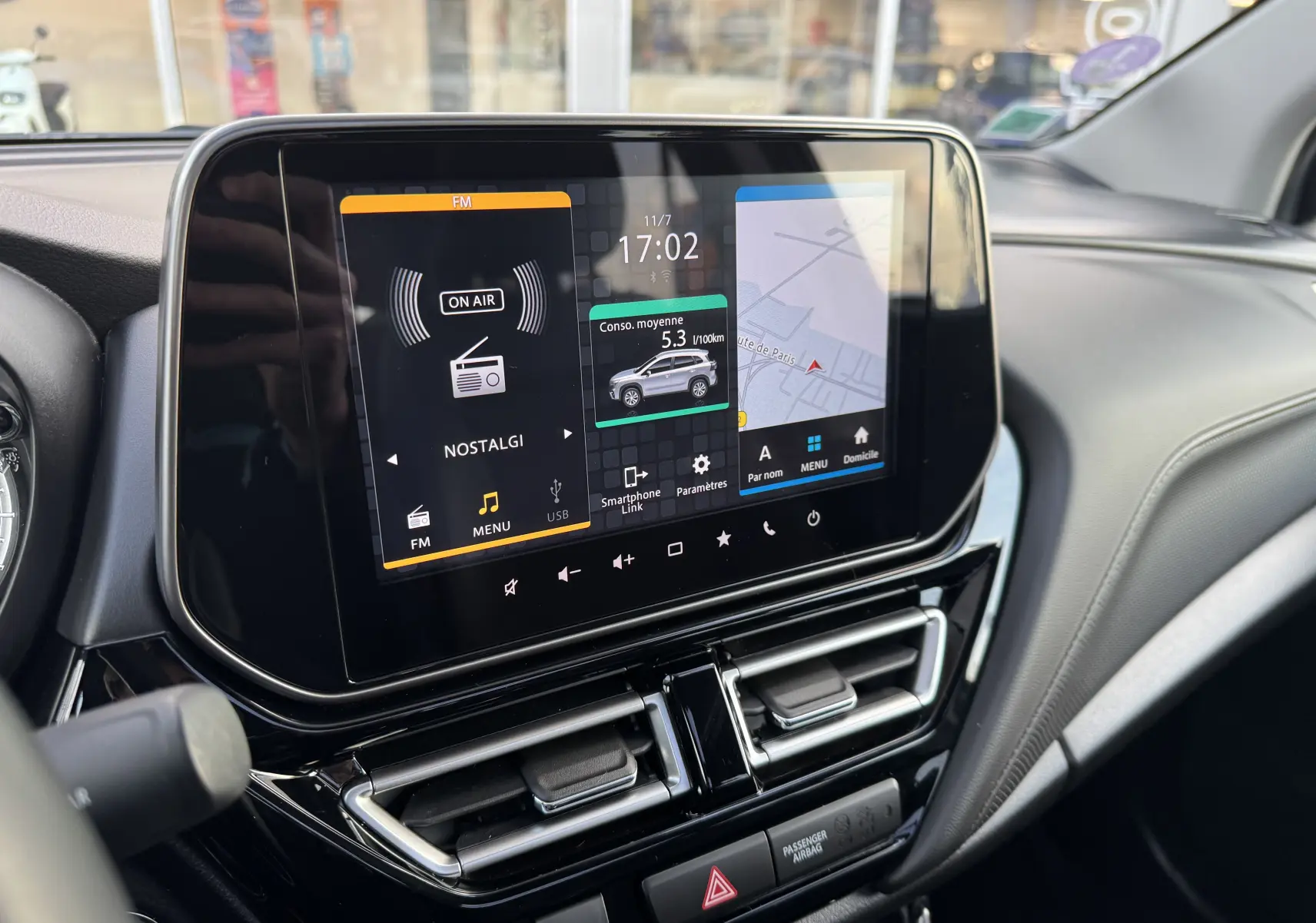 Écran tactile central du tableau de bord du Suzuki S-Cross blanc 2023 affichant radio, consommation et navigation.