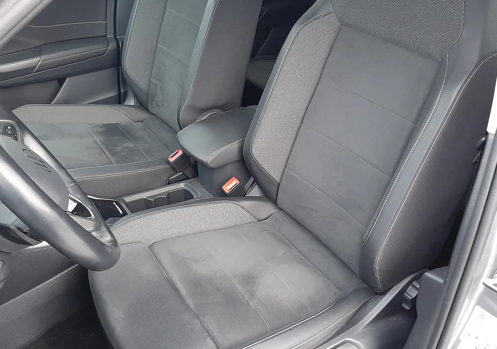 Vue intérieure côté conducteur du Volkswagen T-Roc gris pyrite 2023, sièges noirs en tissu et alcantara, volant multifonction visible.