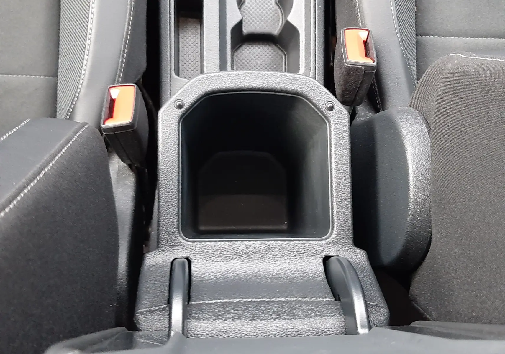 Vue plongeante sur l'accoudoir central noir et la console entre les sièges avant du Volkswagen T-Roc gris Pyrite 2023.