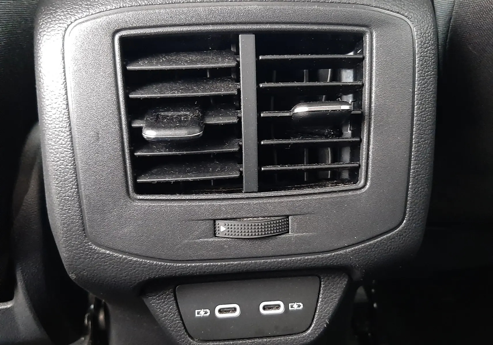 Vue plongeante sur la console centrale noire du Volkswagen T-Roc 2023, avec porte-gobelets et ceintures rouges visibles.