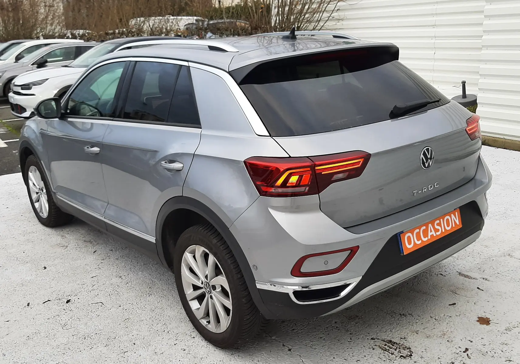 Vue 3/4 arrière droit d'un Volkswagen T-Roc gris pyrite 2023 avec vitres arrière surteintées et jantes alliage.