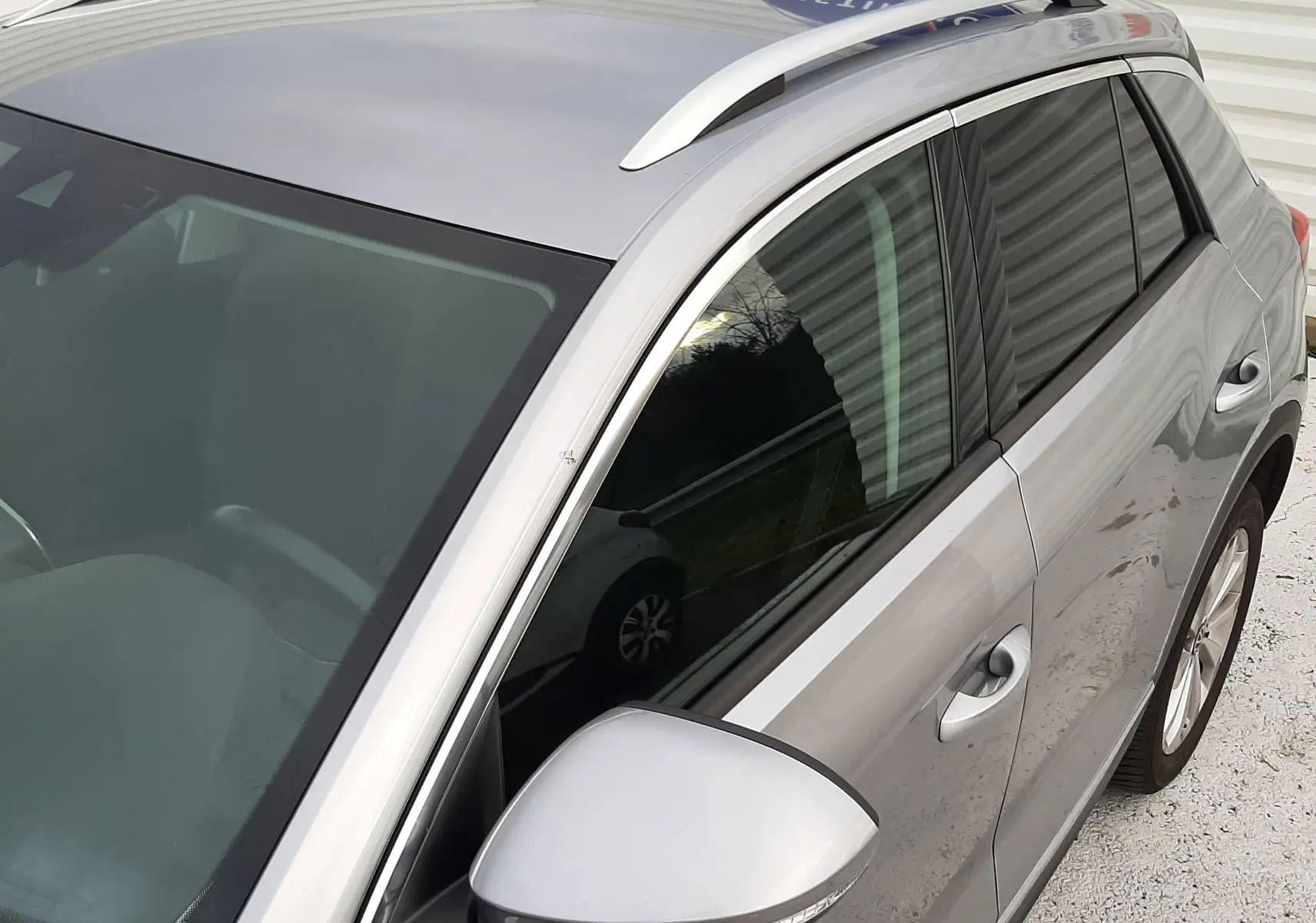 Vue de profil côté gauche d'un Volkswagen T-Roc gris pyrite avec vitres arrière surteintées, stationné sur sol clair.